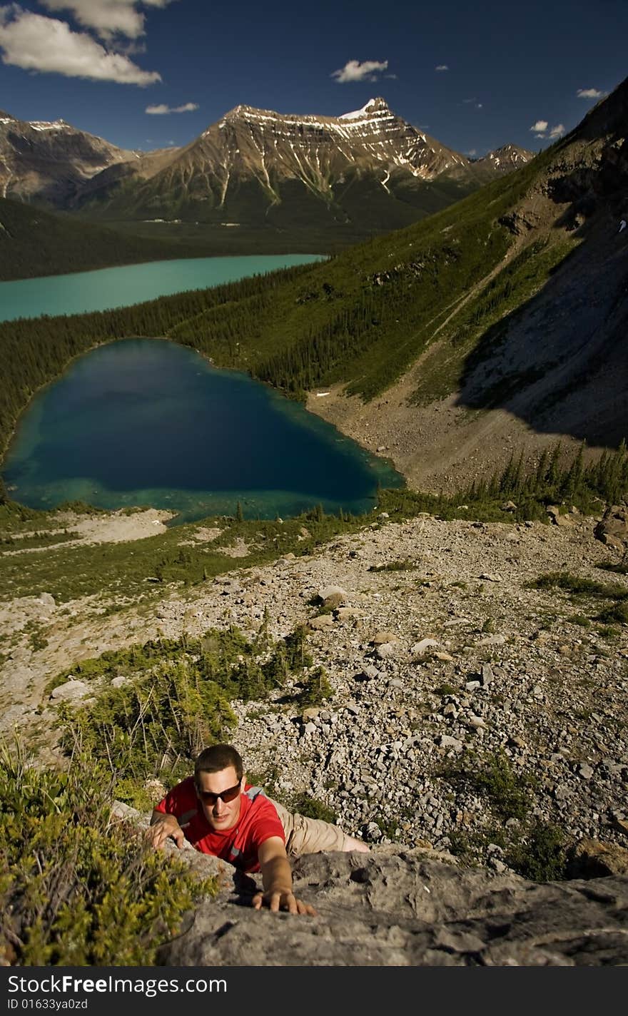 Young climber reaches for handhold on boulder, with turquoise alpine lakes in the background,  Canadian Rocky Mountains. Young climber reaches for handhold on boulder, with turquoise alpine lakes in the background,  Canadian Rocky Mountains