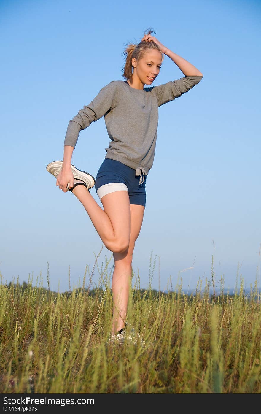Athletics young woman stretching in a hilly meadow.