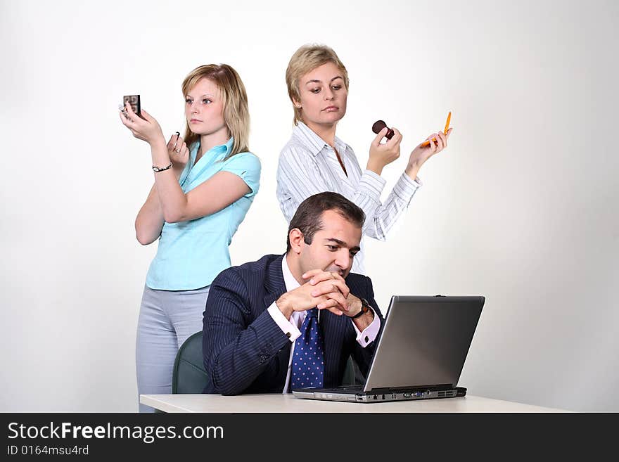 Business make-up. Pretty businesswomen applying make up, when their male colleague is working hard