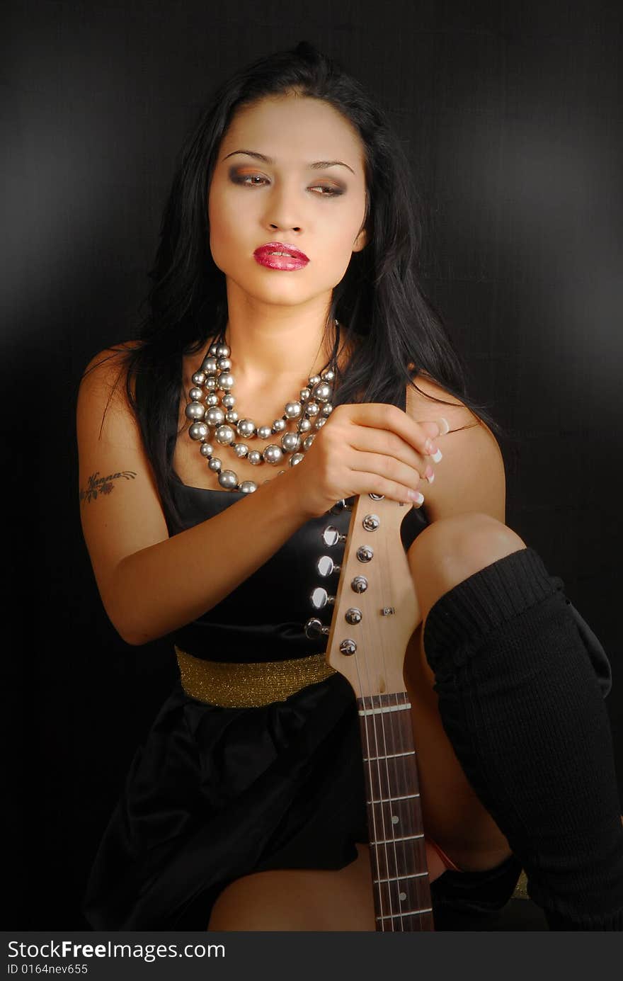 Attractive hispanic female rocker with guitar and dramatic lighting. Attractive hispanic female rocker with guitar and dramatic lighting