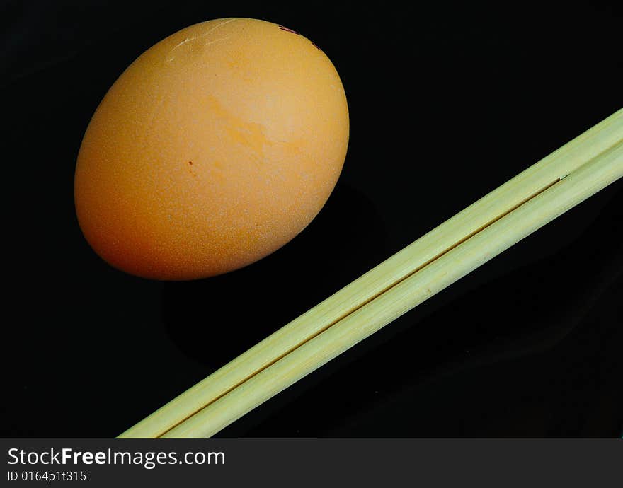 Irony asian diet concept - raw and little bit - egg on black plate and chopsticks. Irony asian diet concept - raw and little bit - egg on black plate and chopsticks