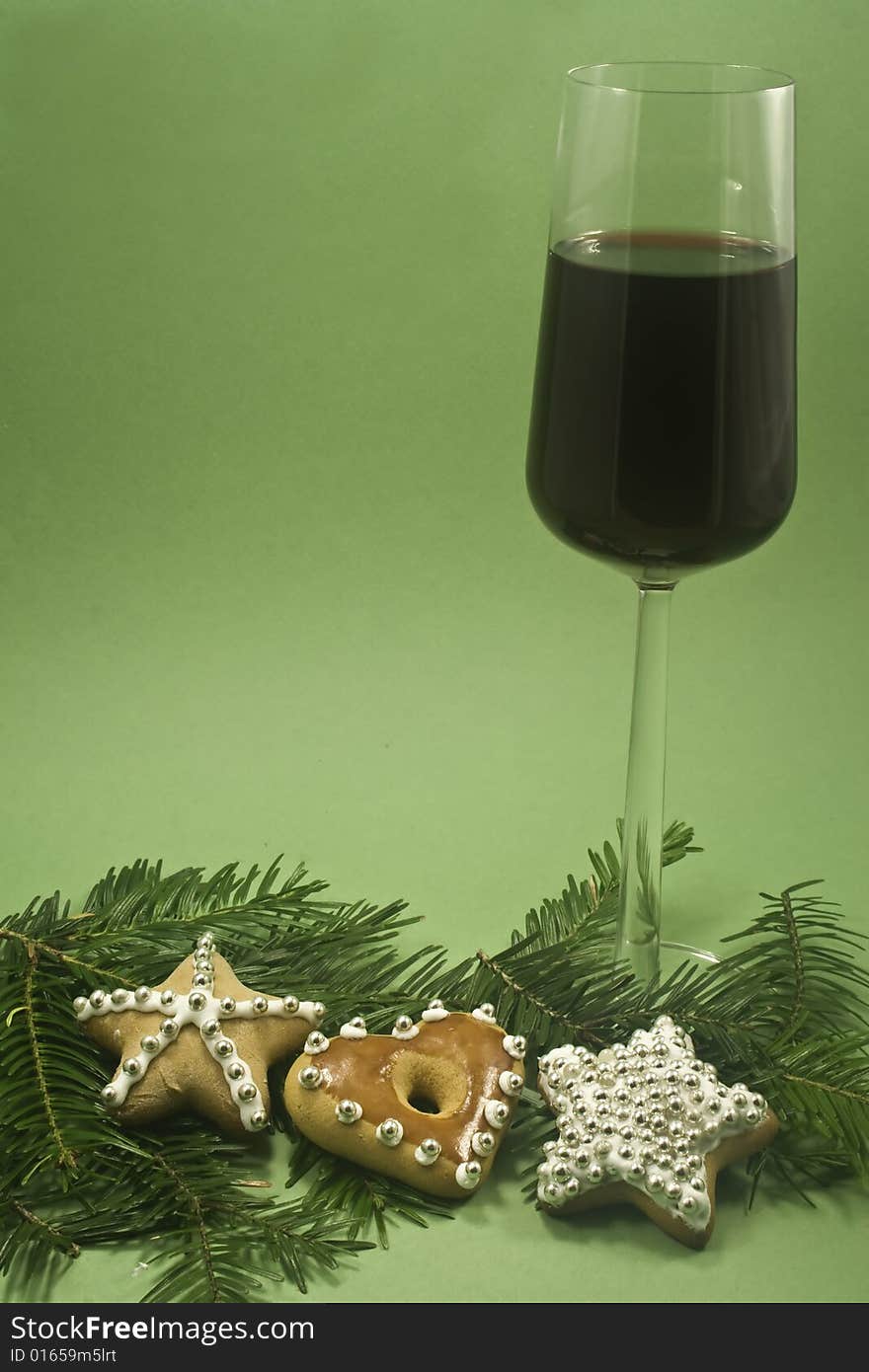 A glass of red wine and three decorated cookies with fir branch isolated on green paper. A glass of red wine and three decorated cookies with fir branch isolated on green paper