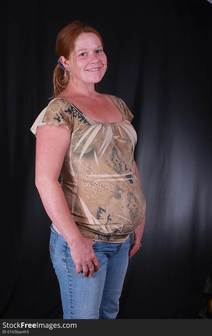 Young women with her hands in her jeans on a black background with a baby in her tummy. Young women with her hands in her jeans on a black background with a baby in her tummy