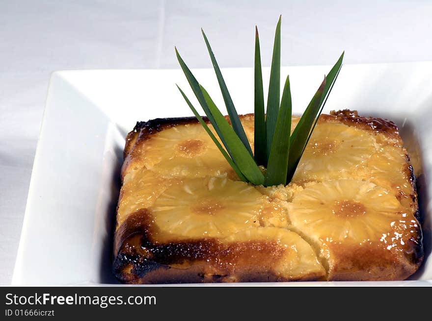 A dish of upside down pineapple pudding. Ingredients include pineapple, milk, syrup, butter, flour and eggs.