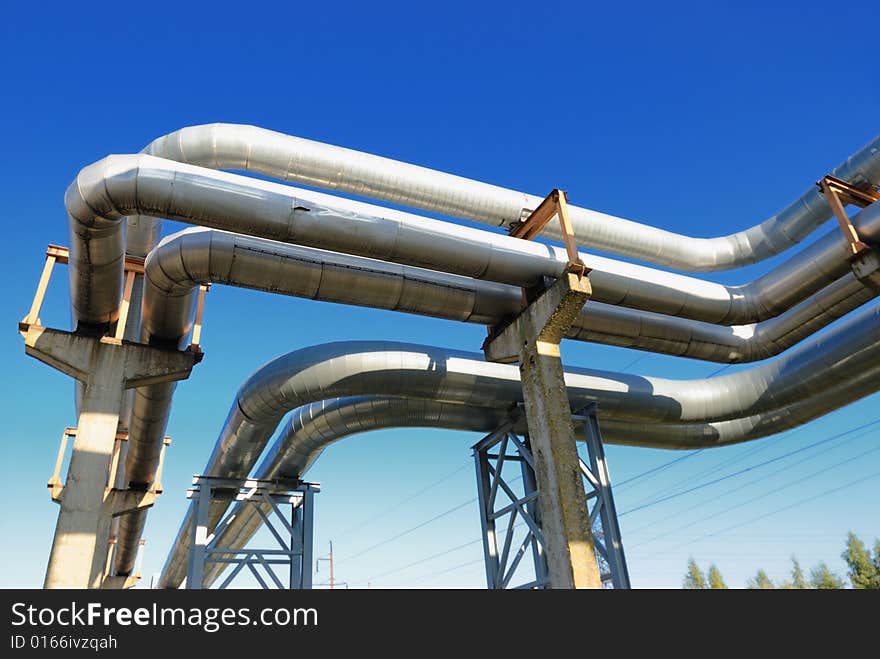 Industrial pipelines on pipe-bridge against blue sky.