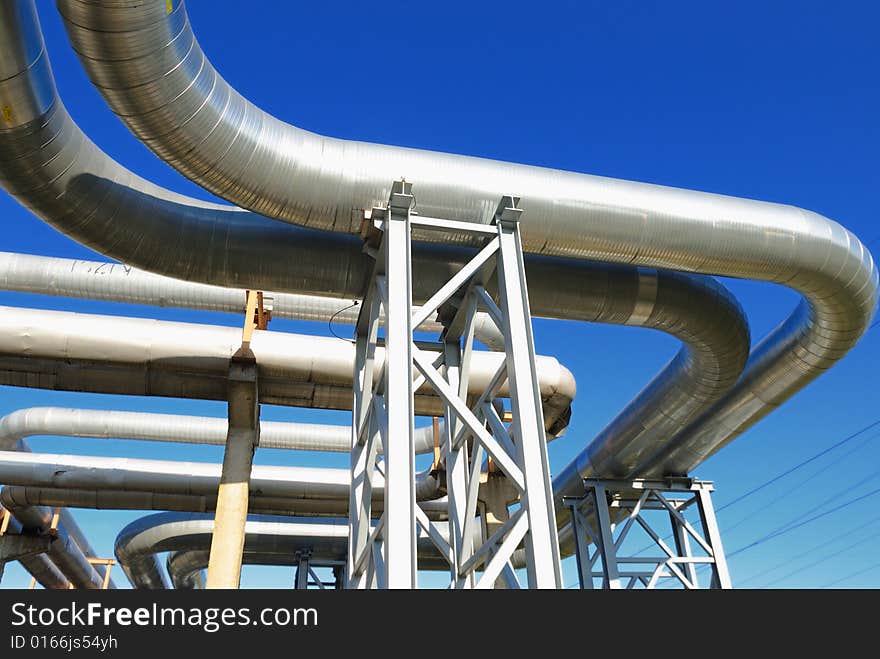 Industrial pipelines on pipe-bridge against blue sky.