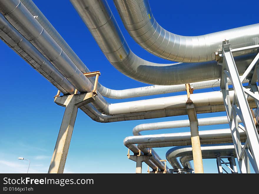 Industrial pipelines on pipe-bridge against blue sky.