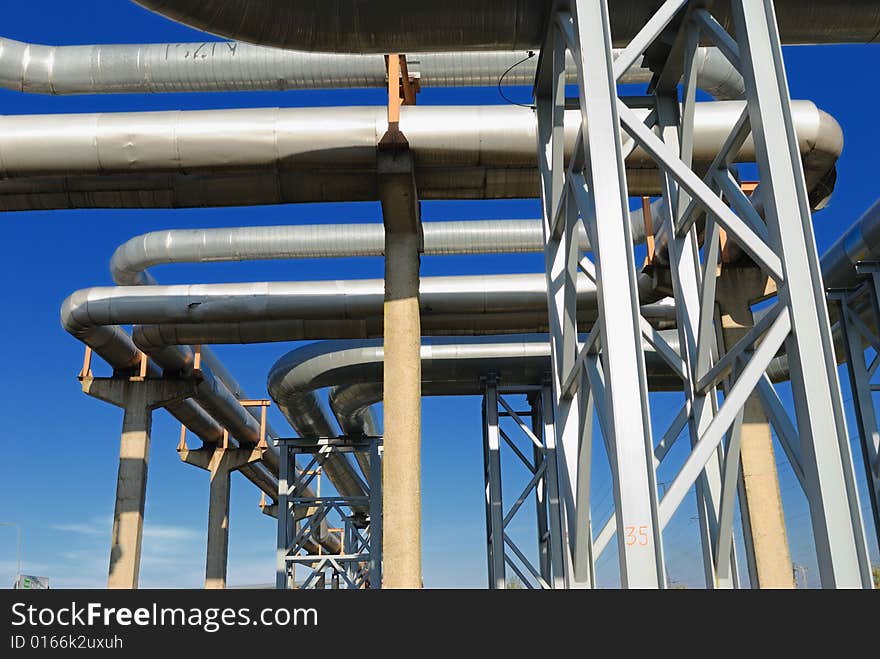 Industrial pipelines on pipe-bridge against blue sky.