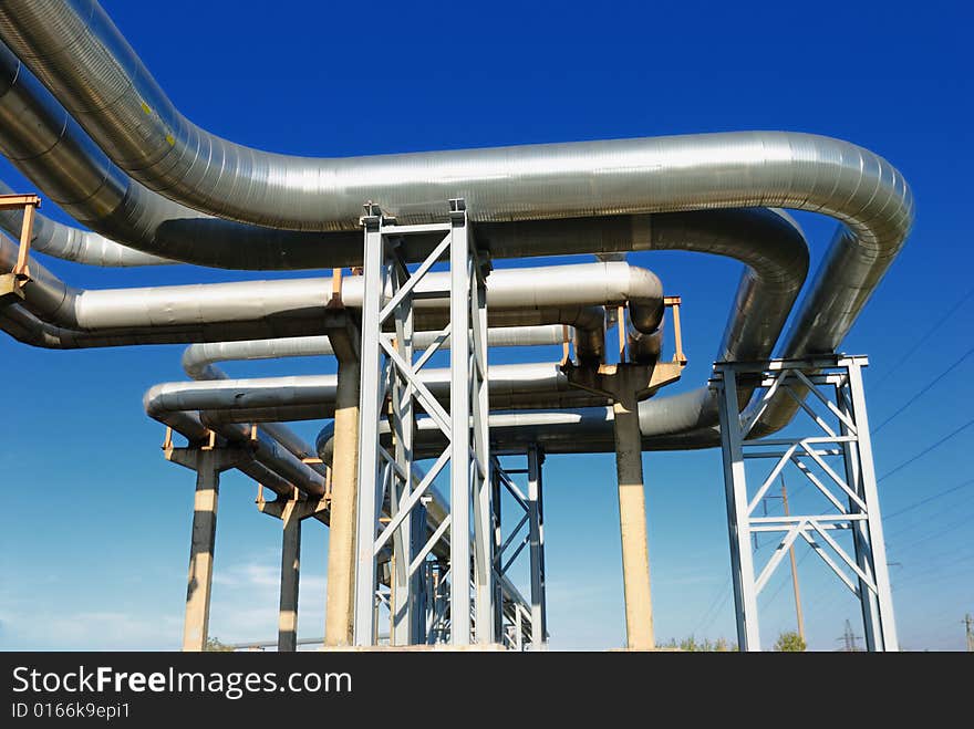 Industrial pipelines on pipe-bridge against blue sky.