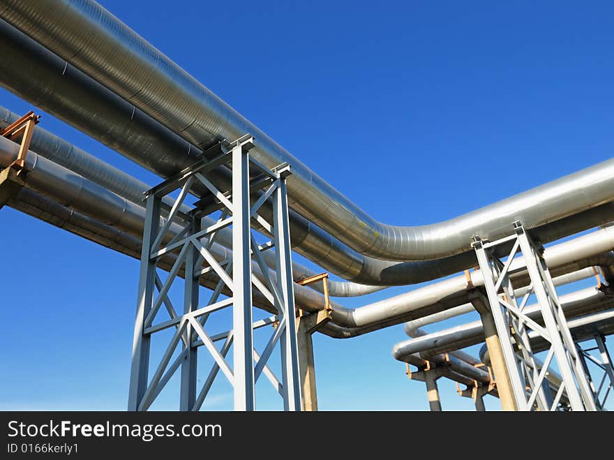 Industrial pipelines on pipe-bridge against blue sky.