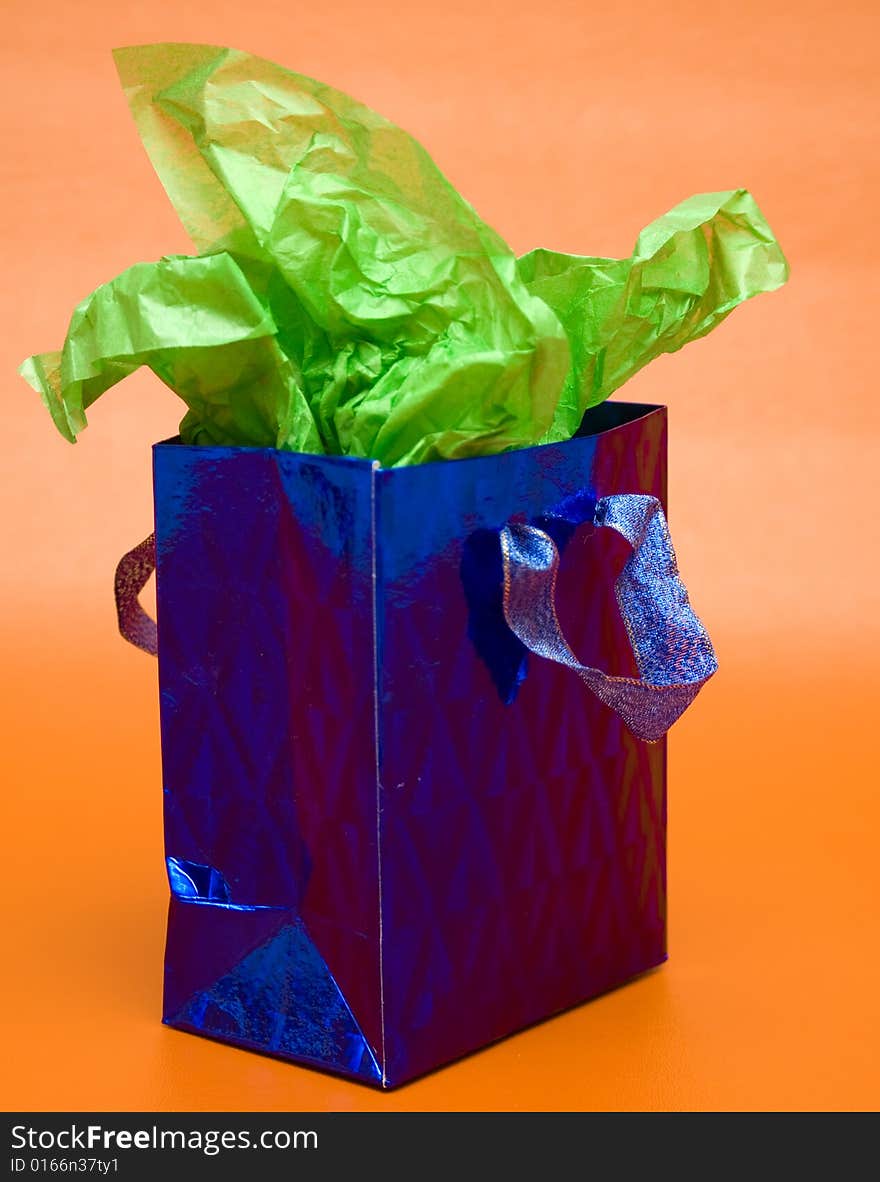 Shiny blue gift bag with green tissue paper against an orange background.