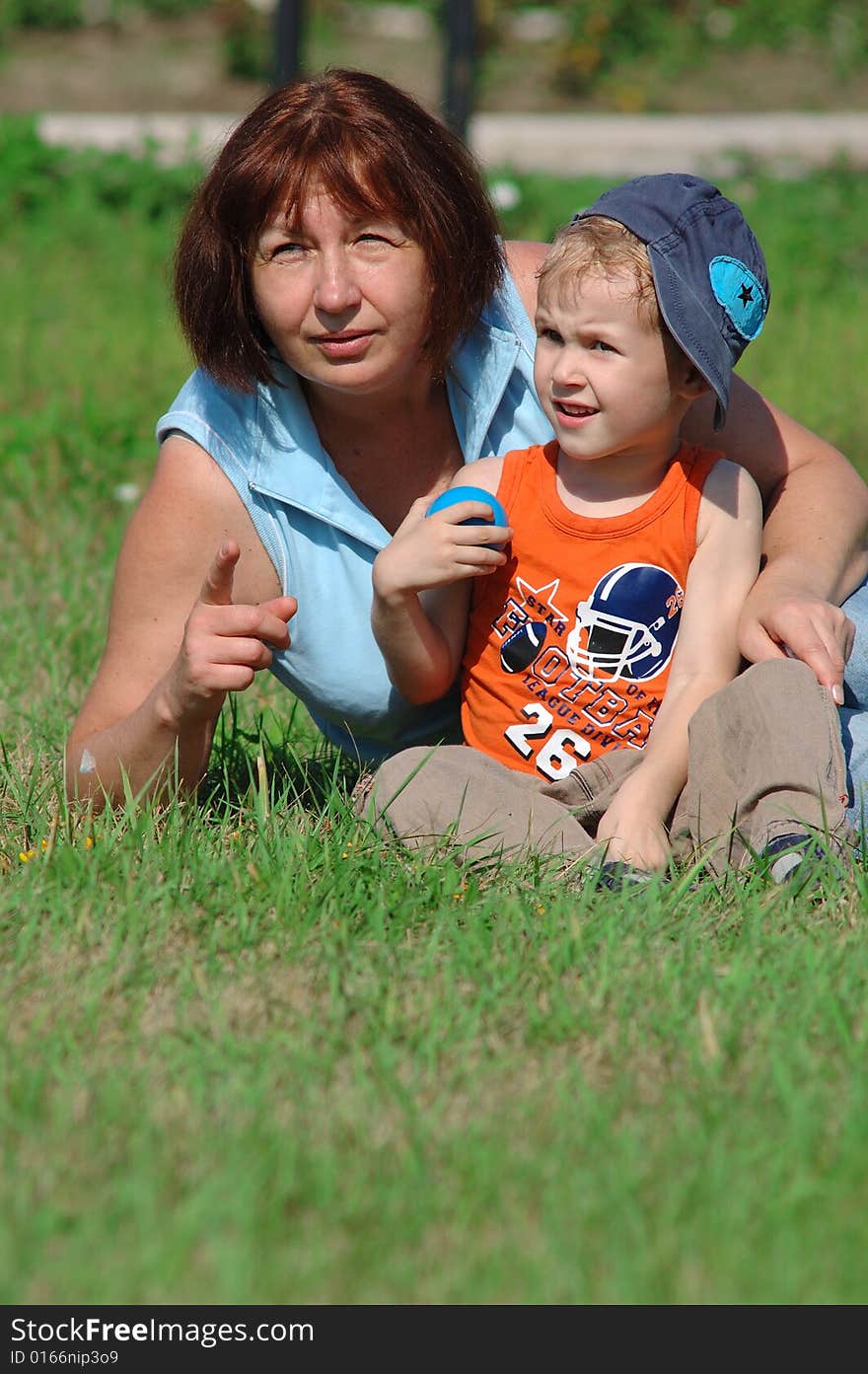 Grandmother and grandson are sitting on the green grass