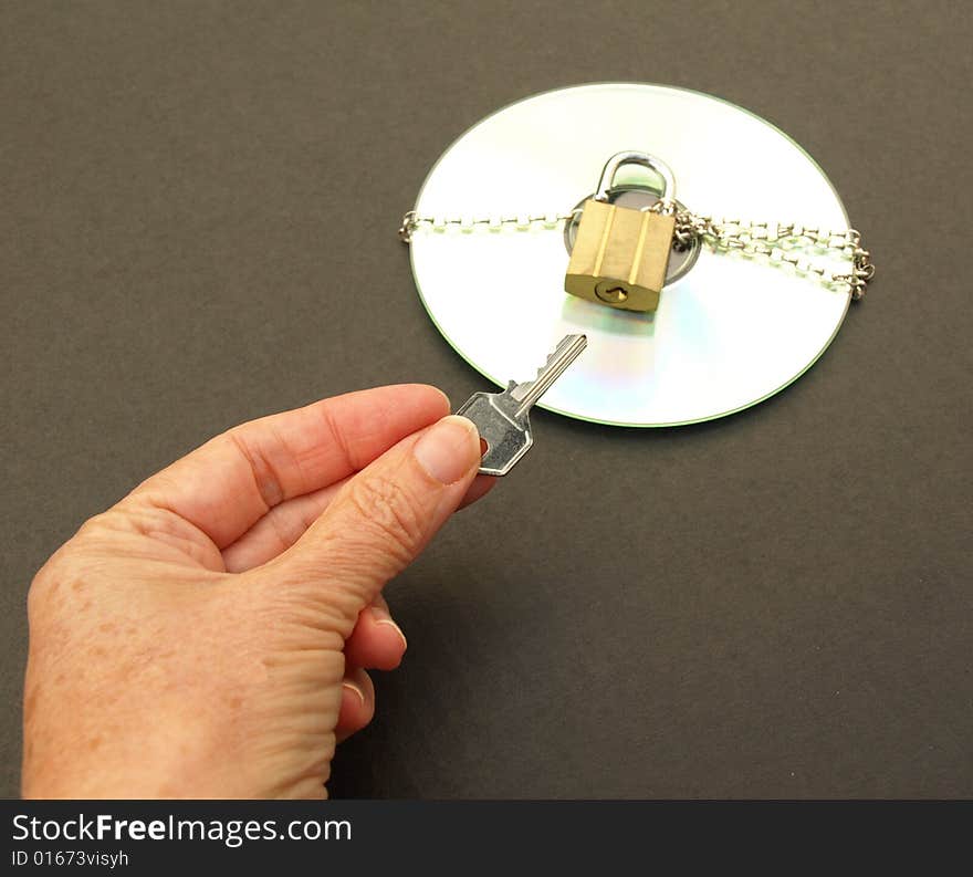 Photograph of hand holding a key and a CD with chain and padlock. Dark background. Photograph of hand holding a key and a CD with chain and padlock. Dark background.