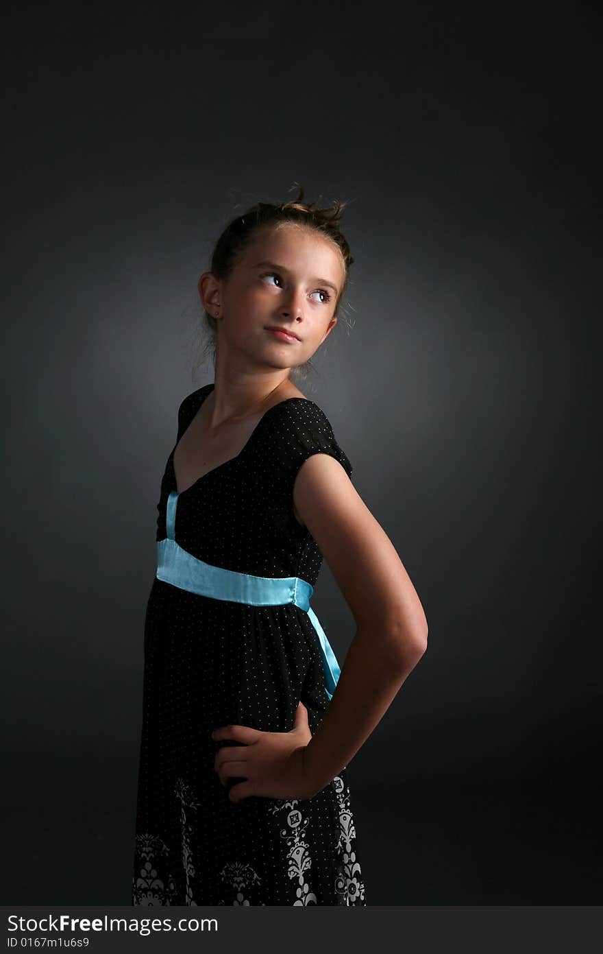 Pretty girl in black dress with blue ribbon standing with hand on her hip