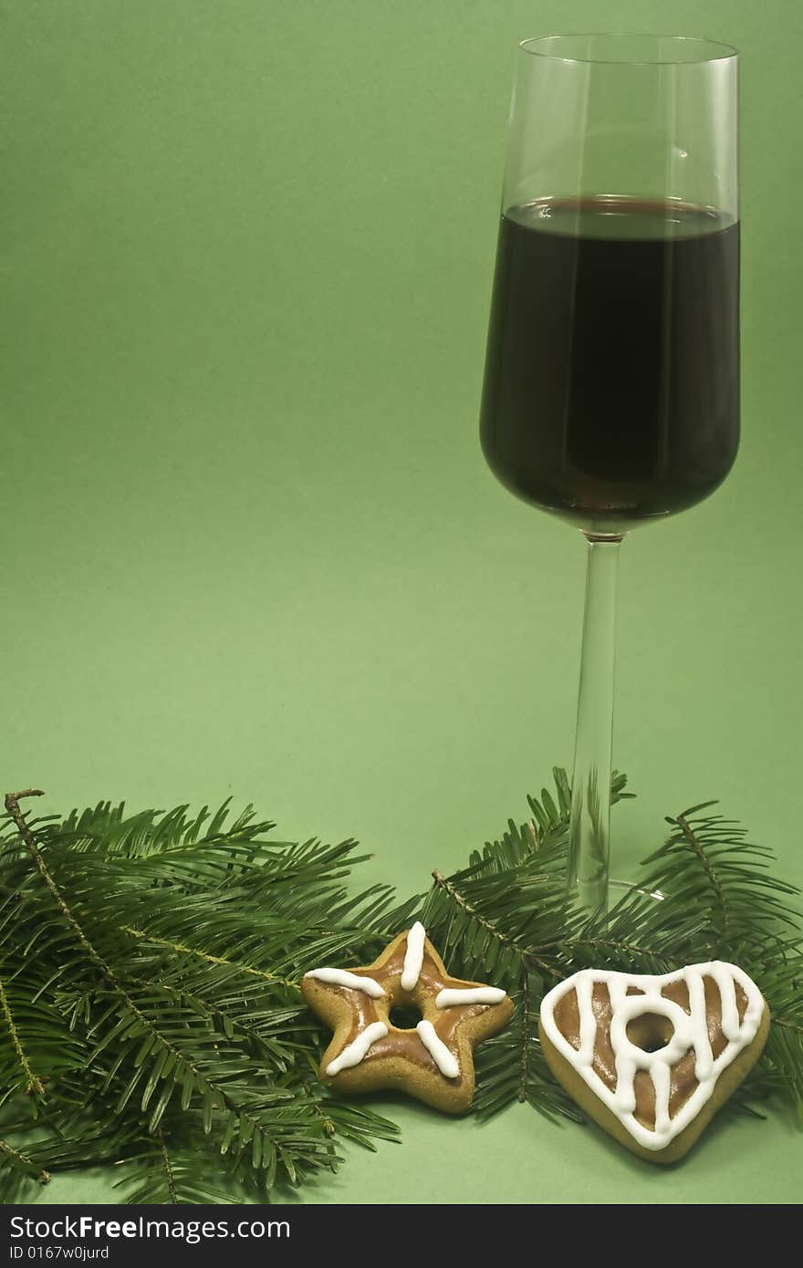 A glass of red wine and two cookies on a fir branch isolated on green paper. A glass of red wine and two cookies on a fir branch isolated on green paper