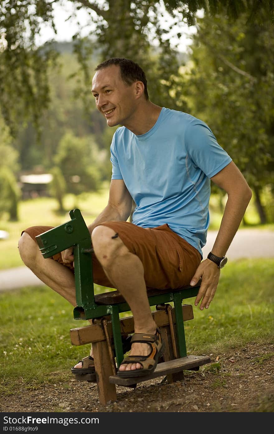 A man enjoying riding a small wooden horse at playground. A man enjoying riding a small wooden horse at playground.