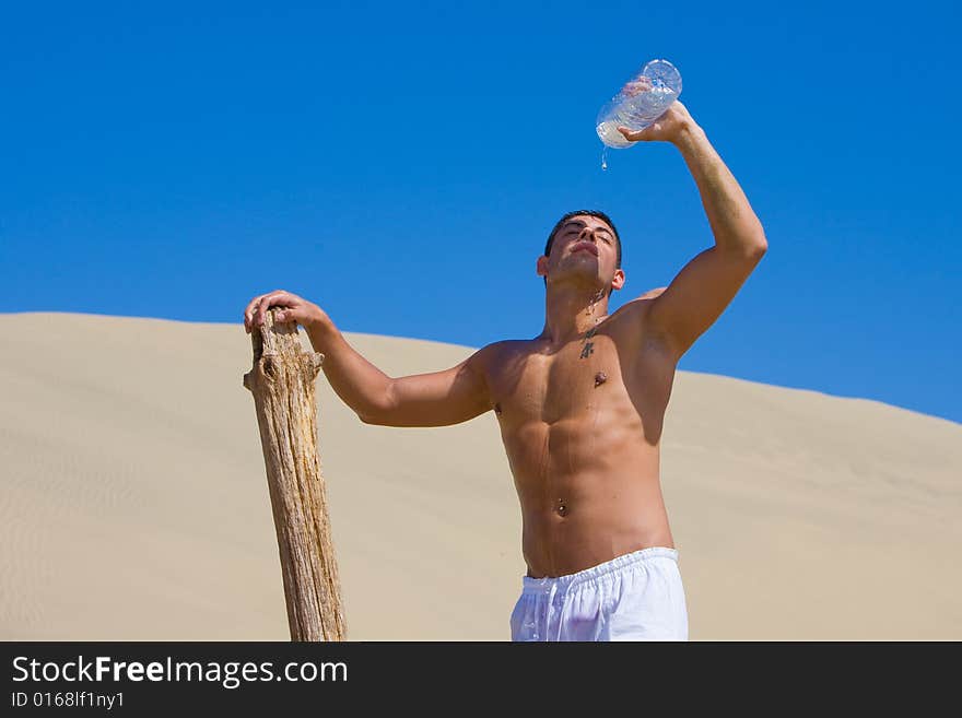 Young atlethic man refreshing with water on desert dune. Young atlethic man refreshing with water on desert dune