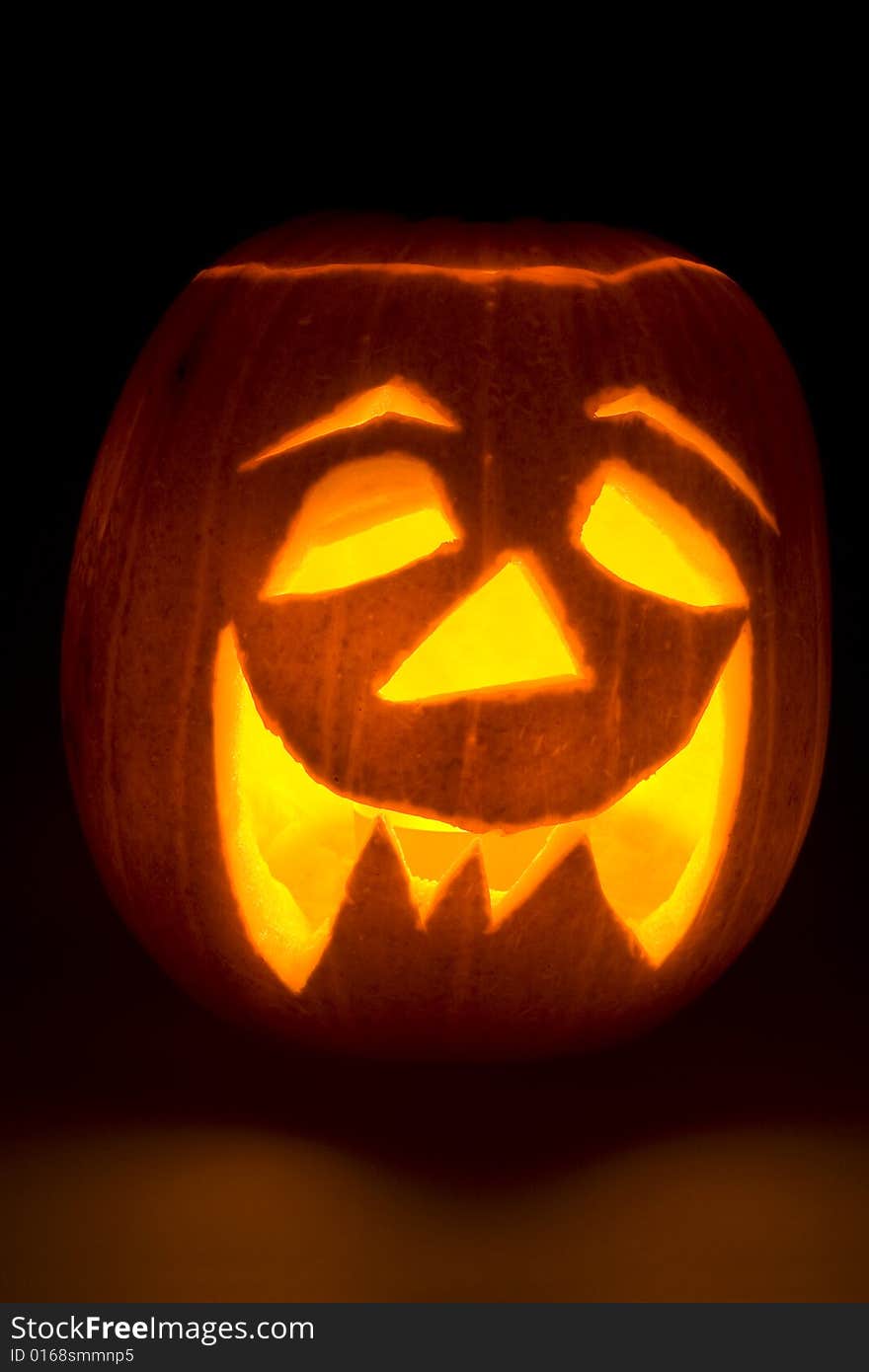 A lighted Halloween 'Jack'o'Lantern' on a dark background with some light spilling into the foreground. A lighted Halloween 'Jack'o'Lantern' on a dark background with some light spilling into the foreground.