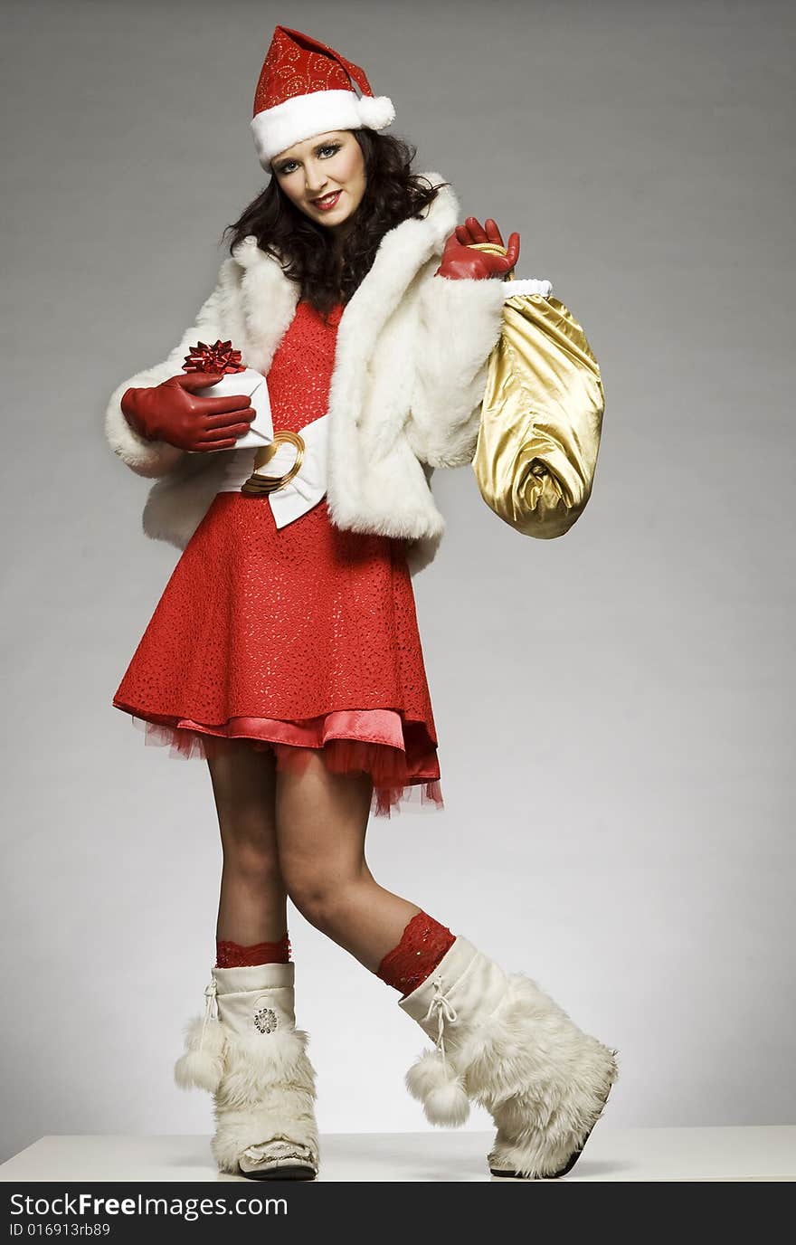 Beautiful brunette girl wearing Santa costume holding Christmas present on grey background. Beautiful brunette girl wearing Santa costume holding Christmas present on grey background