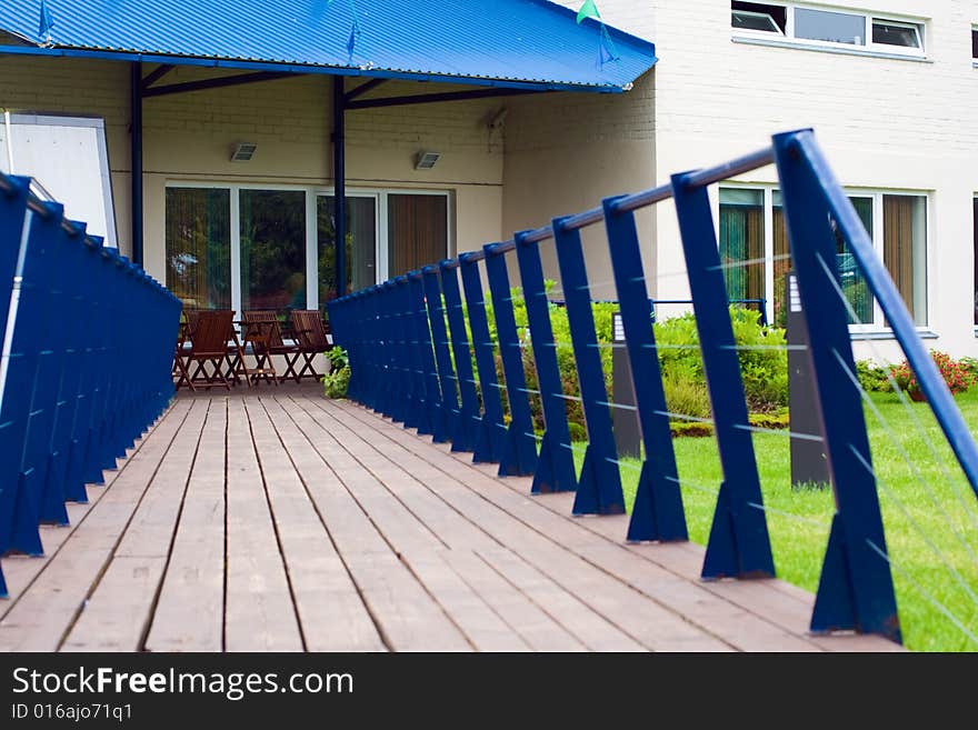 Empty terrace with brown wooden chairs and flooring with blue railing.