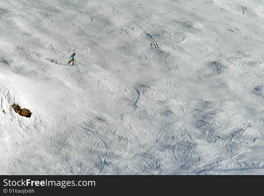 Lone snowboarder going down the hill with lots of tracks on it