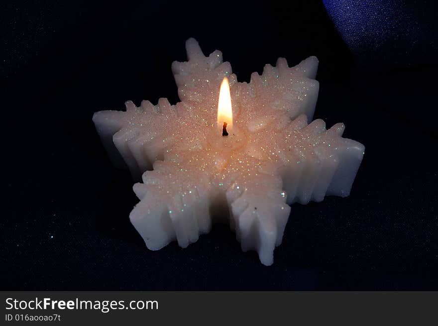 Snowflake-shaped candle on the dark background. Narrow depth of field. Snowflake-shaped candle on the dark background. Narrow depth of field.