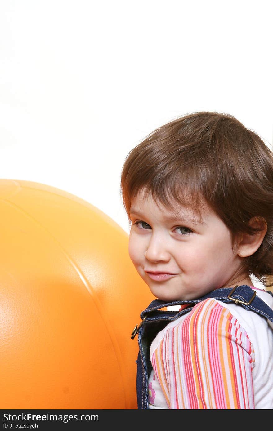 Little girl playing with big orange ball on white ground