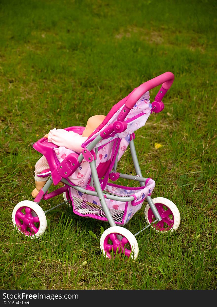 Pink toy pram on green grass