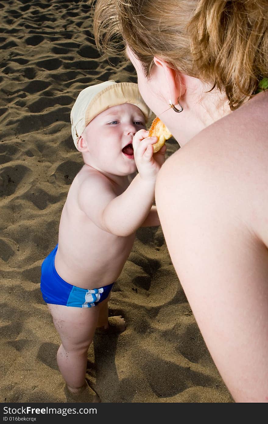 Young child on a beach treats mum with a cake. Young child on a beach treats mum with a cake