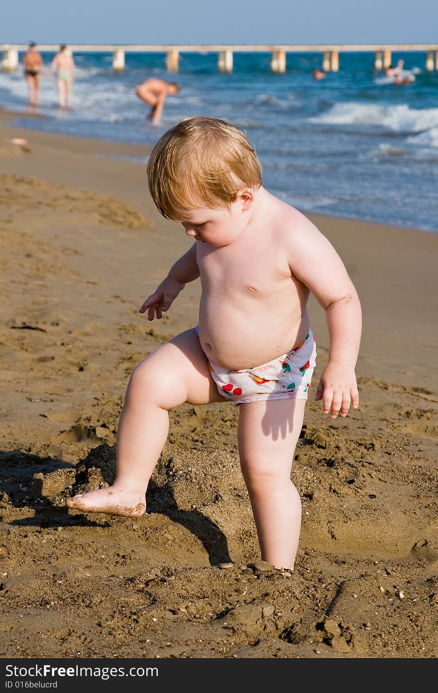 Small child stands on one leg on a beach