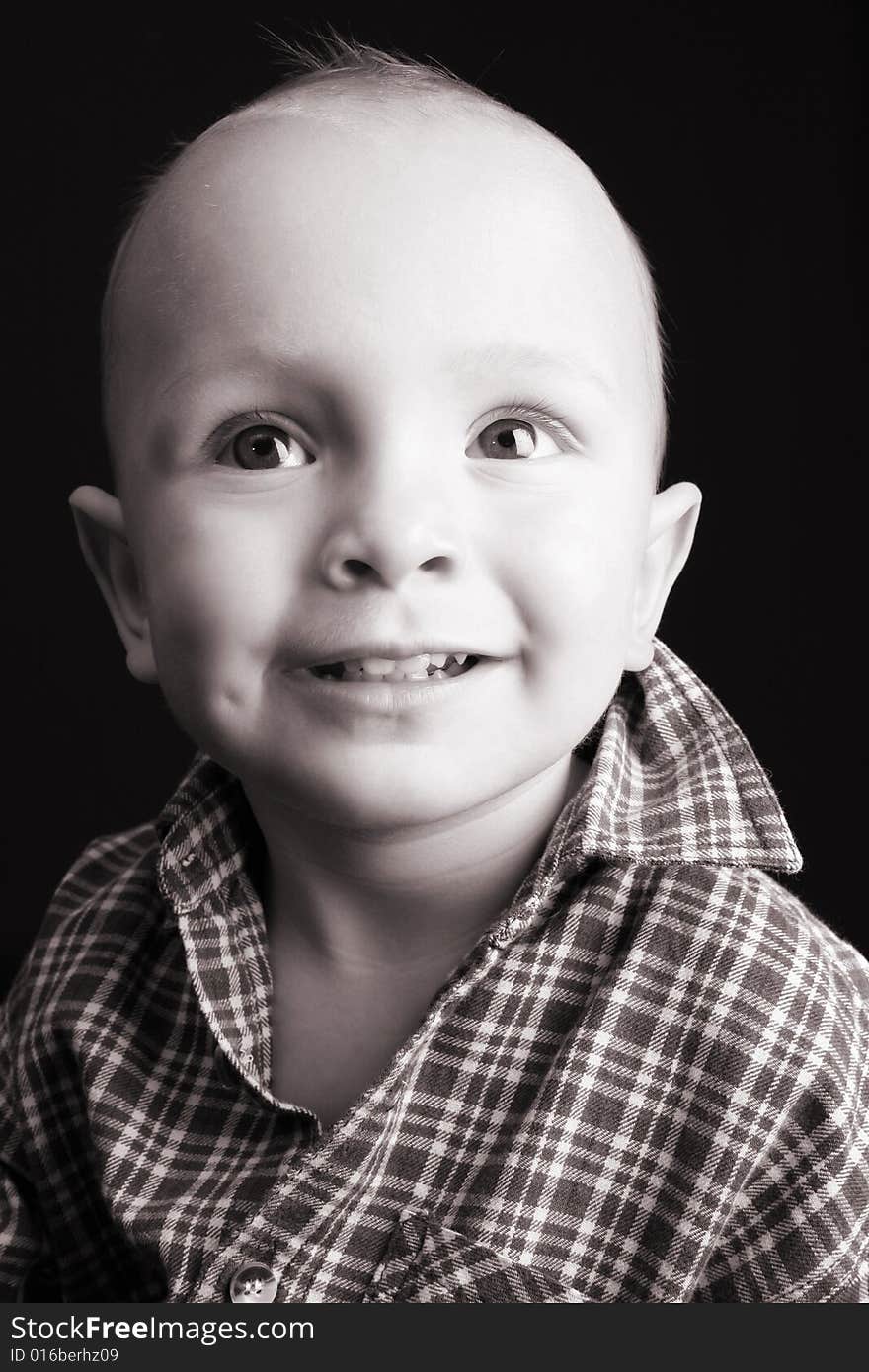 Blonde toddler against a black background with a smile