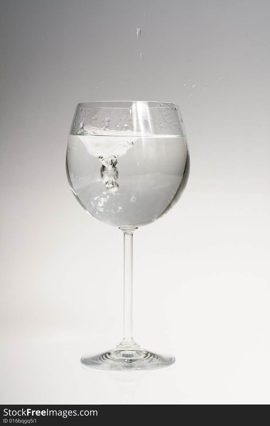 Water splash in wine glass on gradient background from grey to white. Water splash in wine glass on gradient background from grey to white