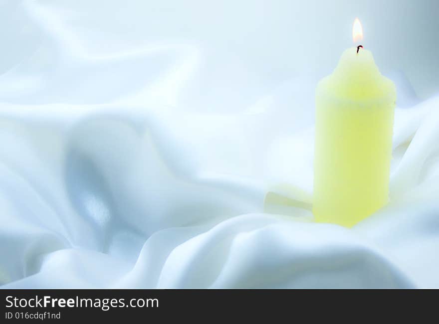 Burning candle on white silk