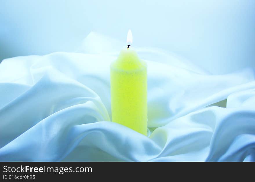 Burning candle on white silk