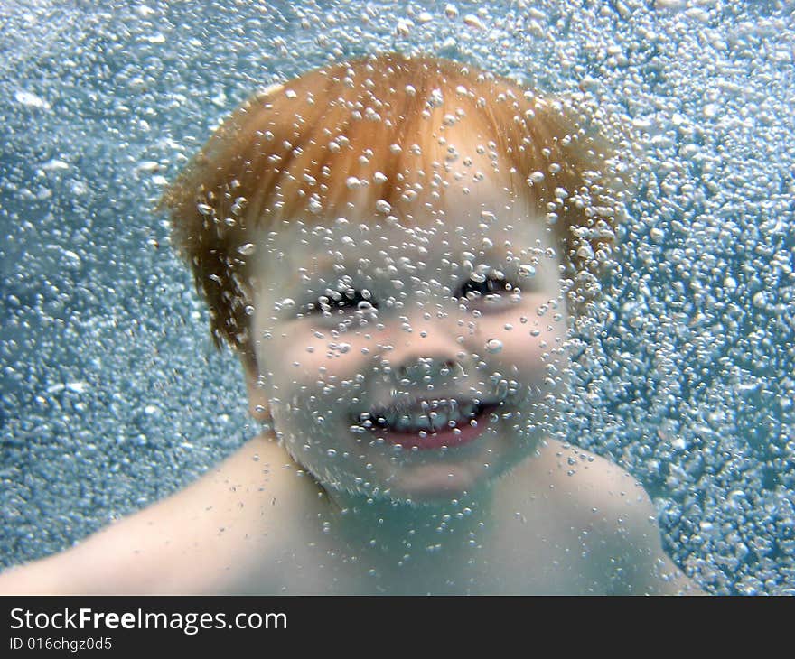 Portrait of a 2 yr old boy jumping into the pool, smiling at the camera through a curtain of bubbles. Portrait of a 2 yr old boy jumping into the pool, smiling at the camera through a curtain of bubbles