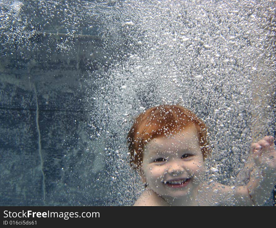 Portrait of a 2 yr old boy jumping into the pool, smiling at the camera through a curtain of bubbles. Portrait of a 2 yr old boy jumping into the pool, smiling at the camera through a curtain of bubbles