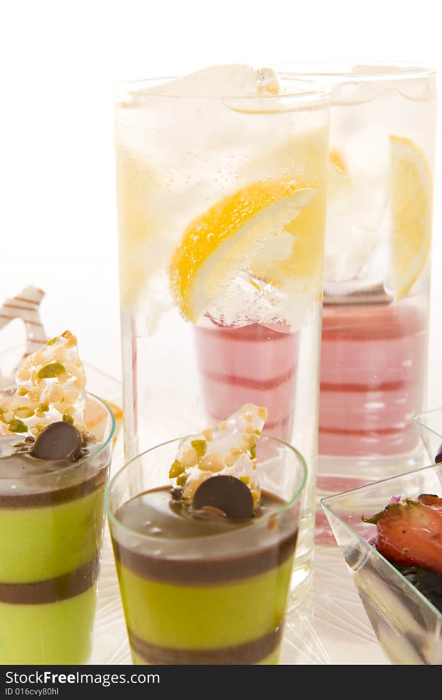 Glasses with sparkling water containing fresh lemon slices, surrounded by colorful confectionery on a white background. Glasses with sparkling water containing fresh lemon slices, surrounded by colorful confectionery on a white background.