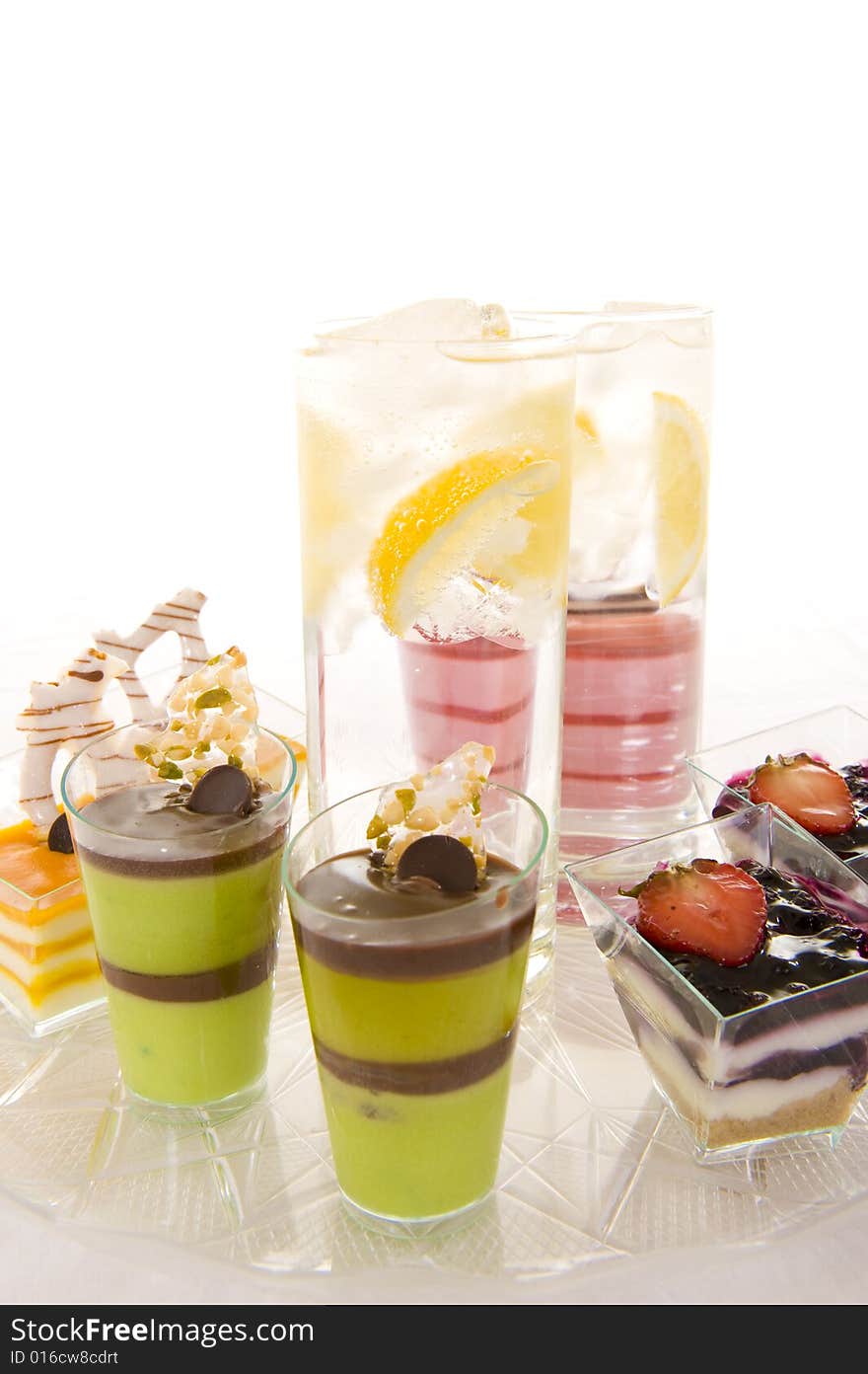 Glasses with sparkling water containing fresh lemon slices, surrounded by colorful confectionery on a white background. Glasses with sparkling water containing fresh lemon slices, surrounded by colorful confectionery on a white background.