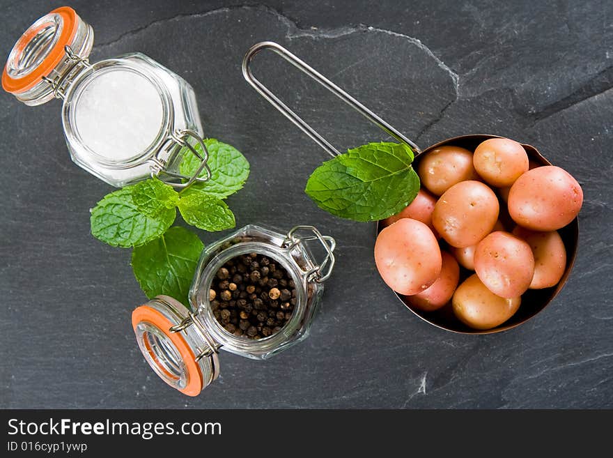 New potatoes in a small pan with salt, pepper and mint on a slate background. New potatoes in a small pan with salt, pepper and mint on a slate background