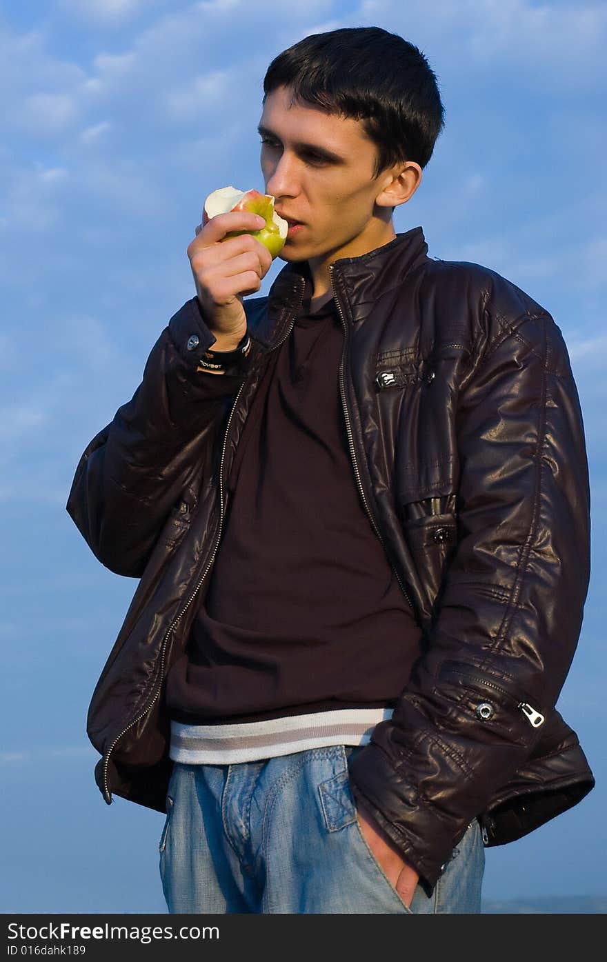 Young man eats an apple against the blue sky