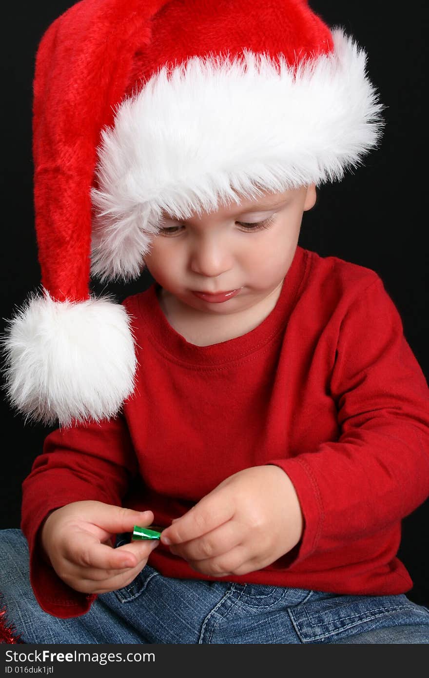 Blonde toddler against a black background with a christmas hat