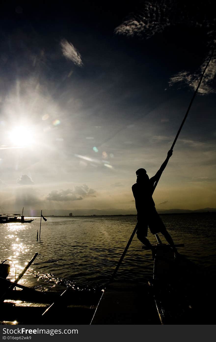 A fisherman steers a small boat with a bamboo poles on shallow water. A fisherman steers a small boat with a bamboo poles on shallow water.