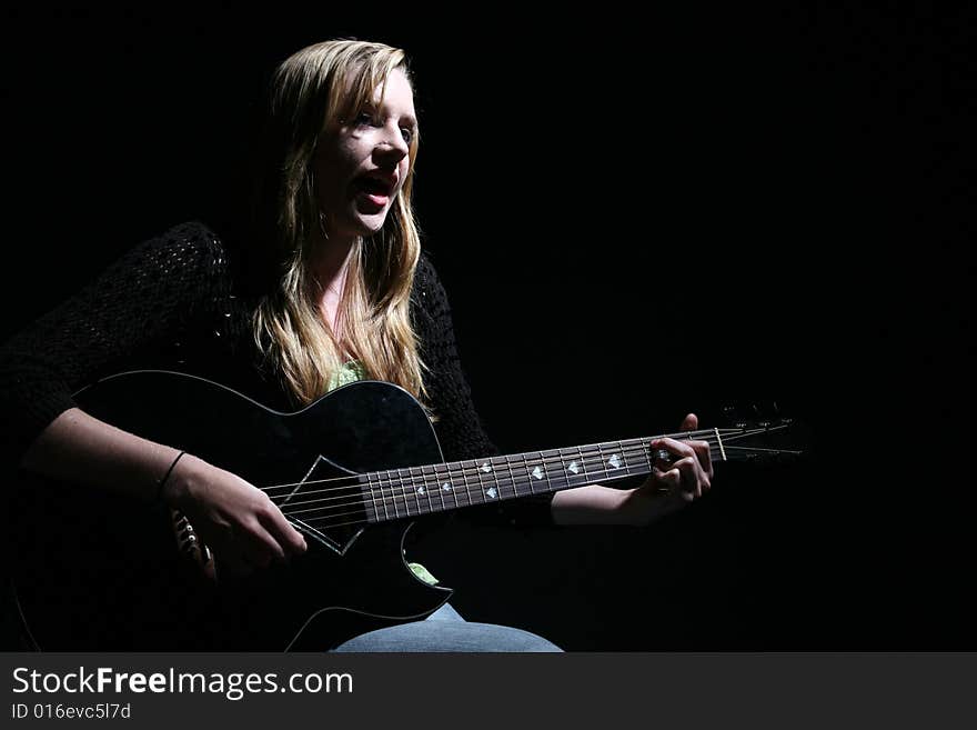 Moody picture of beautiful woman playing guitar and singing