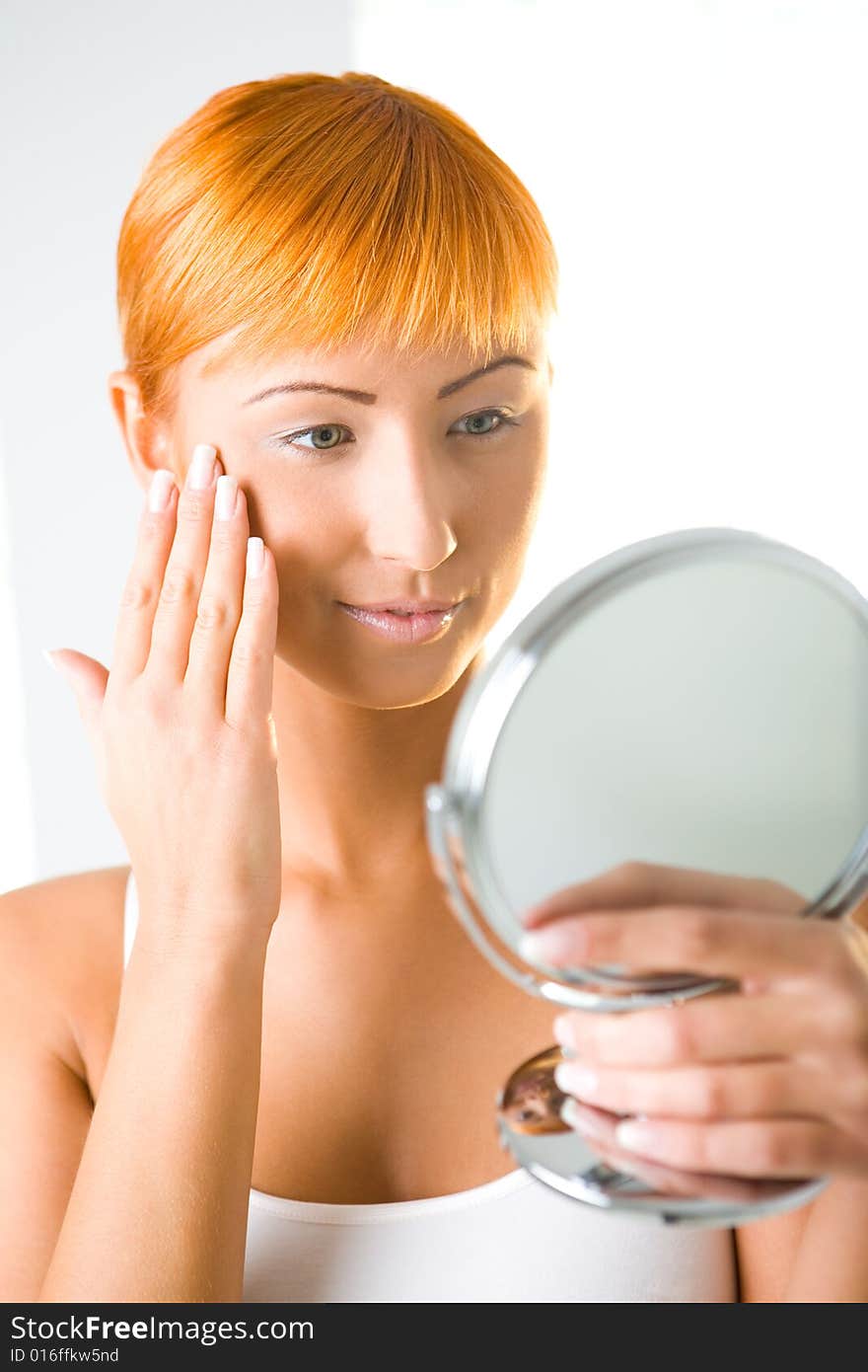 Young woman looking in mirror and touching her face. Front view. Young woman looking in mirror and touching her face. Front view.