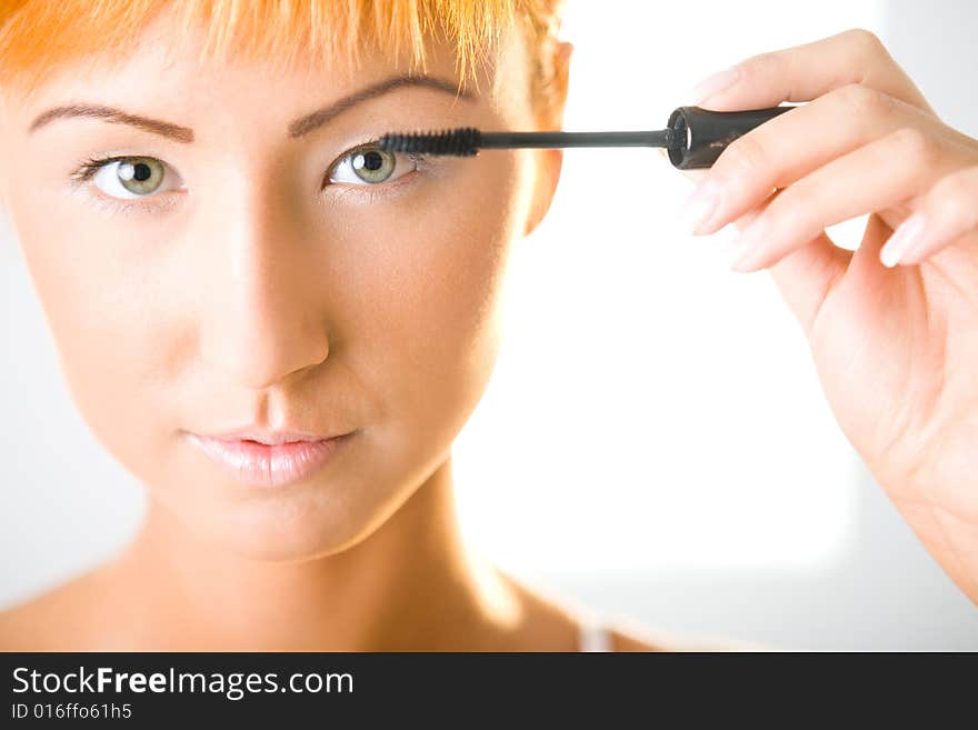 Young woman putting eyelash mascara. She's looking at camera. Closeup on face. Front view. Young woman putting eyelash mascara. She's looking at camera. Closeup on face. Front view.