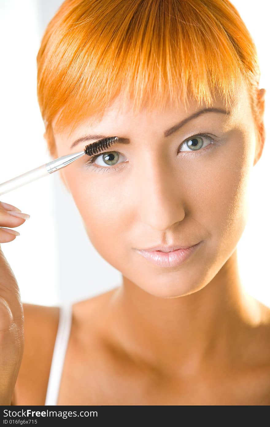 Young woman making her makeup. She's looking at camera. Closeup on face. Front view. Young woman making her makeup. She's looking at camera. Closeup on face. Front view.