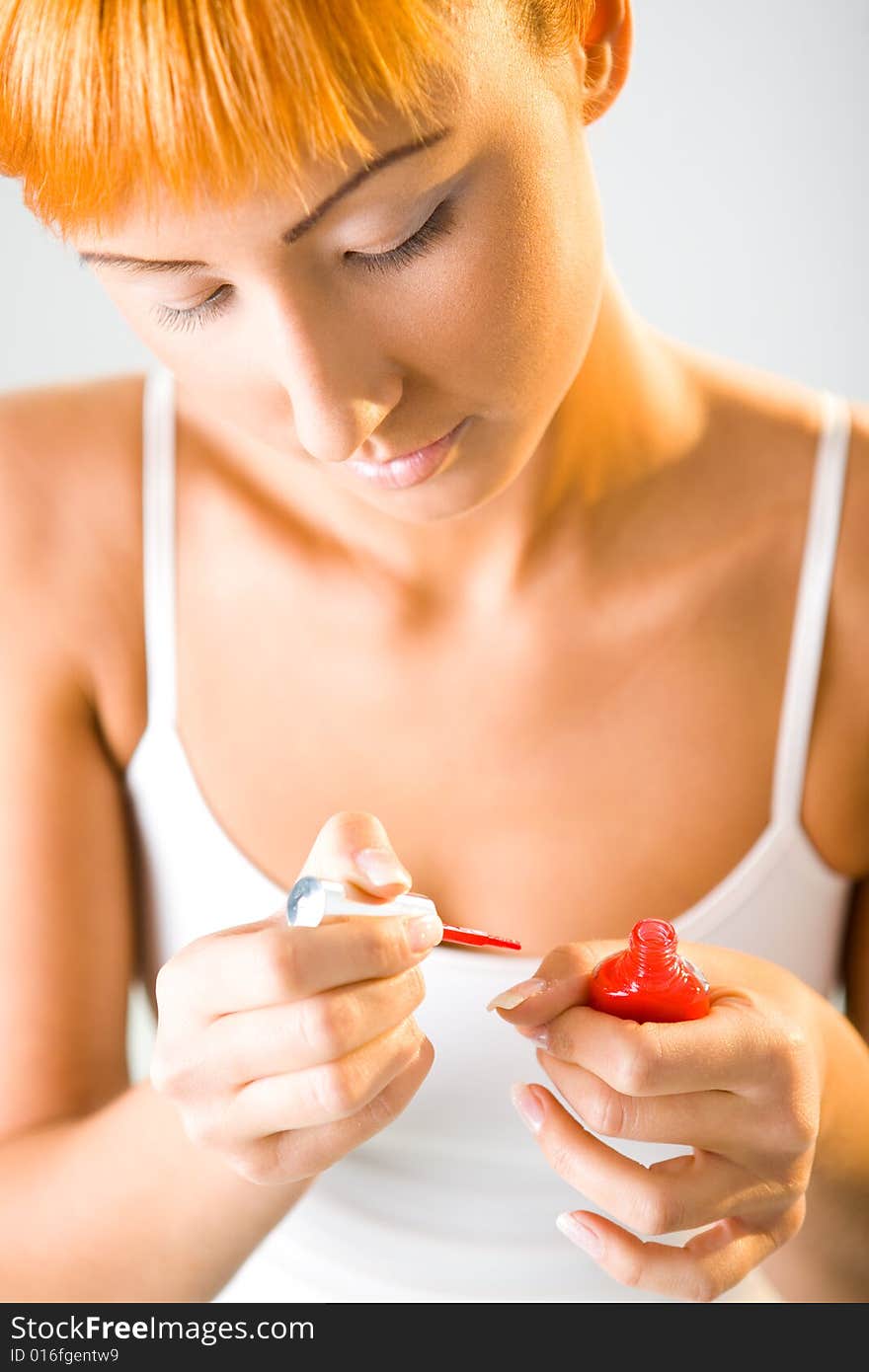 Young woman painting fingernails with red nail varnish. Fokused on hands with brush and bottle with red nail varnish. Front view.