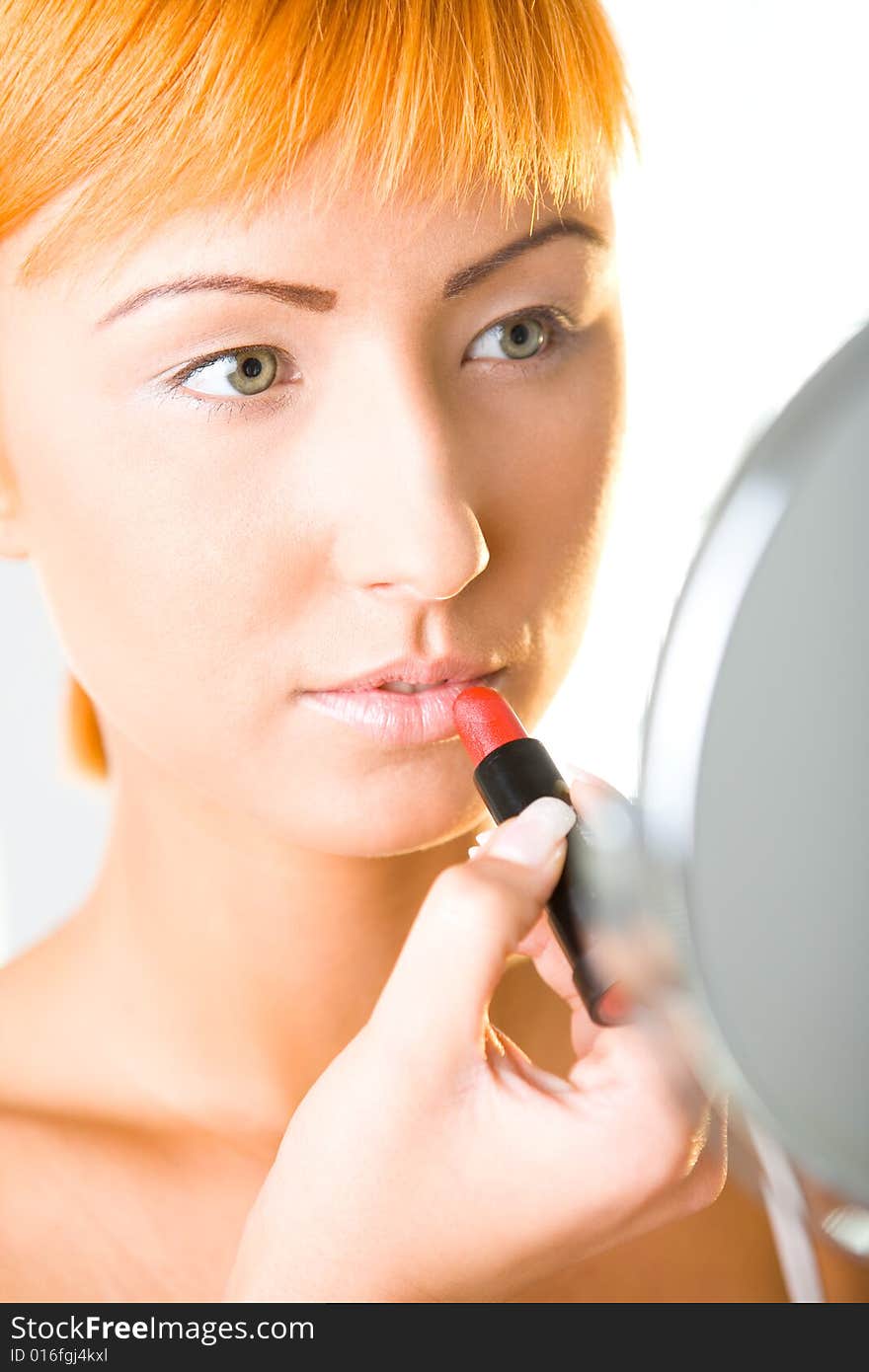 Beautiful woman applying red lipstick. She's looking into mirror. Closeup on face. Beautiful woman applying red lipstick. She's looking into mirror. Closeup on face.