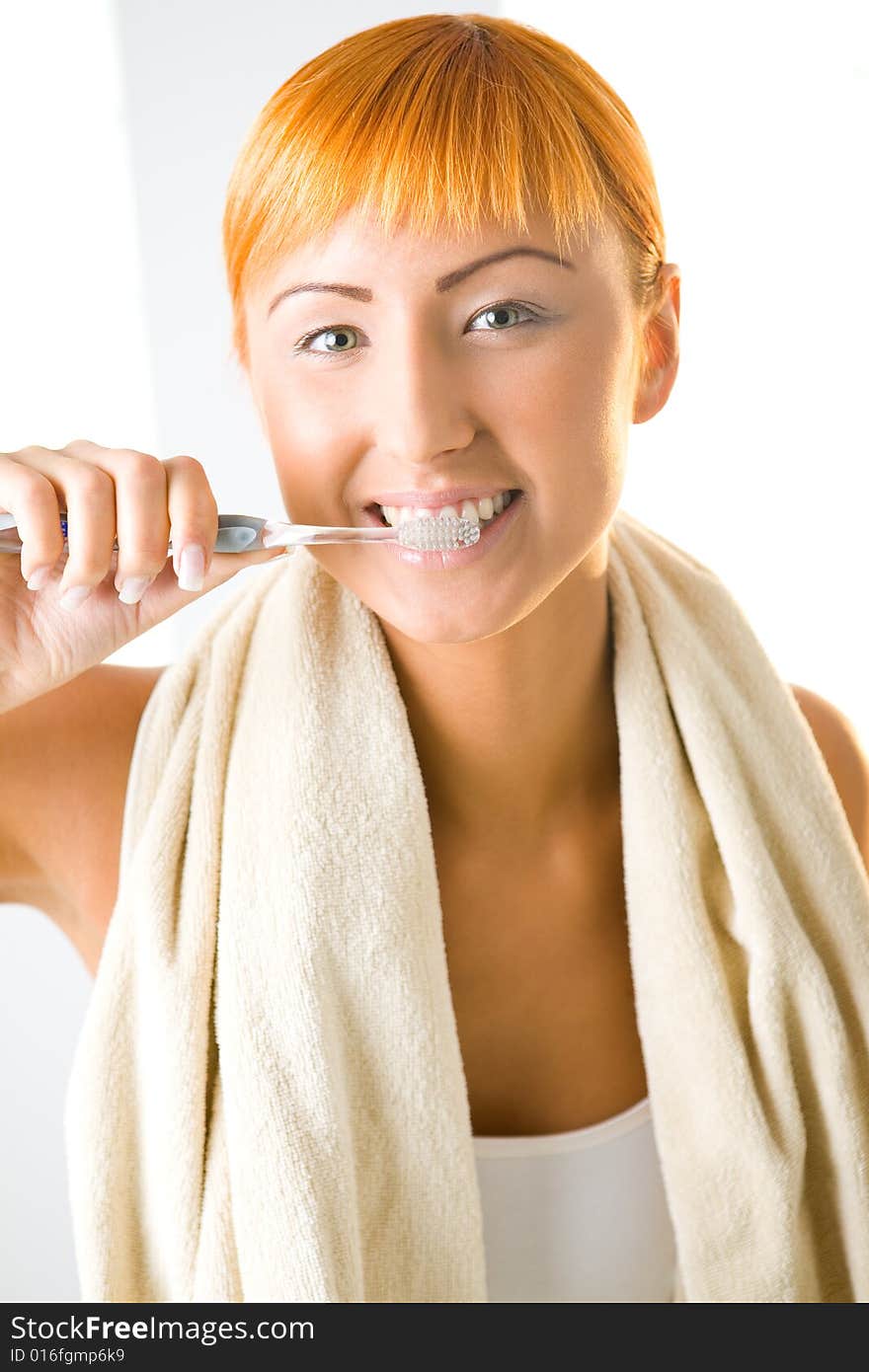 Young beauty woman with toothbrush and towel. She's brushing her teeth and looking at camera. Front view. Young beauty woman with toothbrush and towel. She's brushing her teeth and looking at camera. Front view.