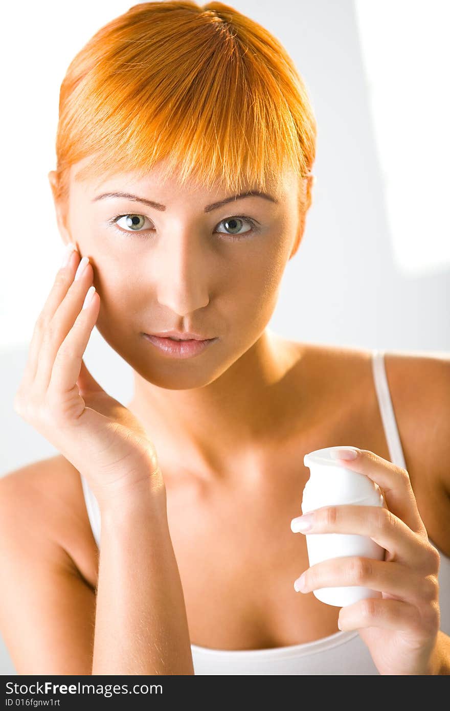 Beauty woman applying face cream. She's looking at camera. Front view.